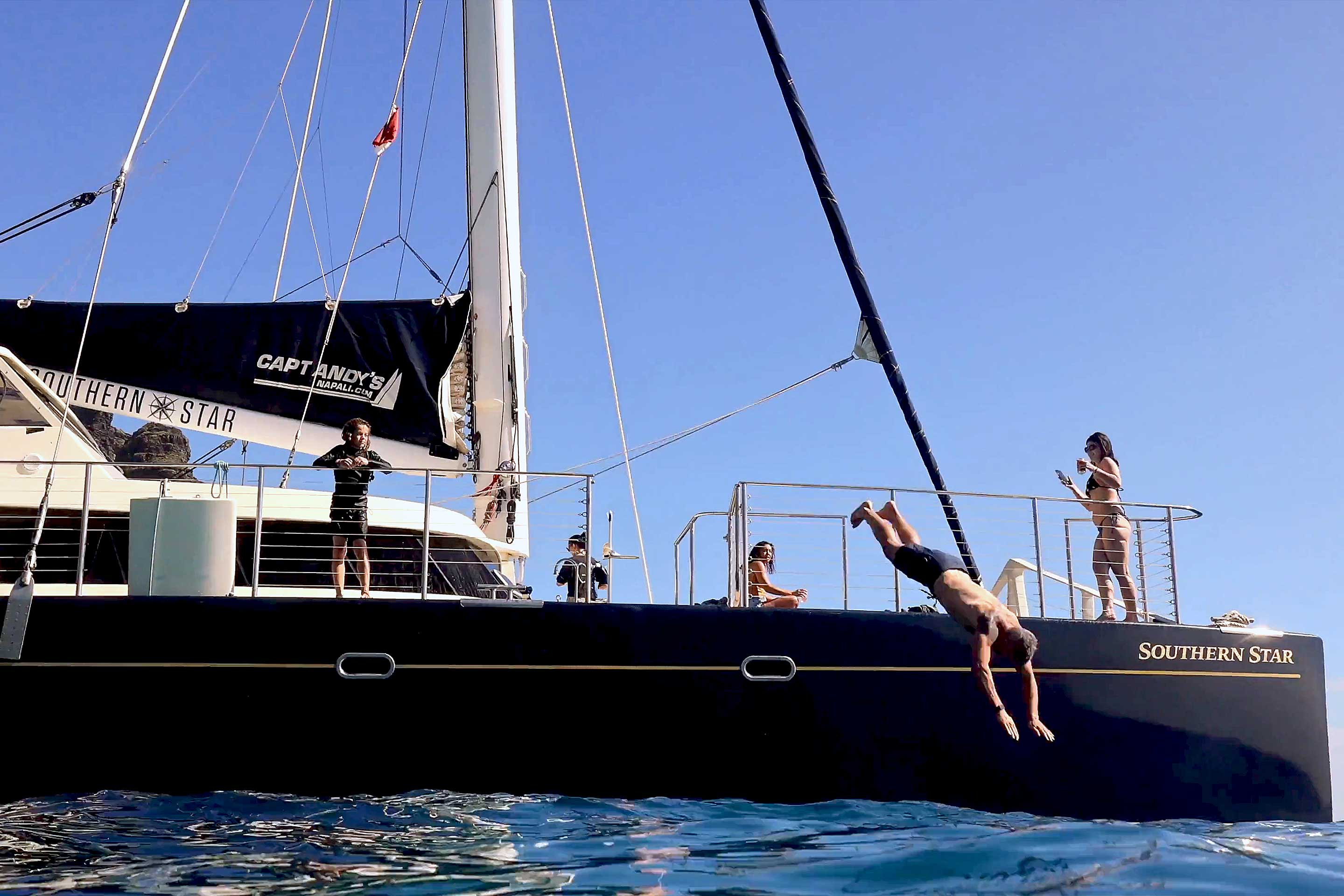 Man diving off a Kauai catamaran into the ocean along the Na Pali Coast.